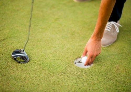 Golf ball, putter and boy's legs on green